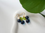 Close-up of handmade blueberry resin dangle earrings with green enamel leaf and white flower