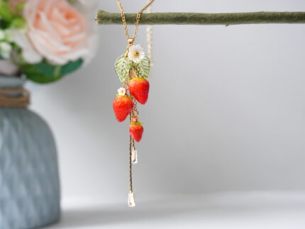 Gold necklace with three handmade polymer clay strawberries, a white flower charm, and green leaves, hanging with two dangling zircon crystal drops