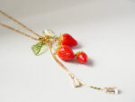 Angled macro shot of polymer clay strawberry charms with a green leaf and crystal drop chain on a textured surface