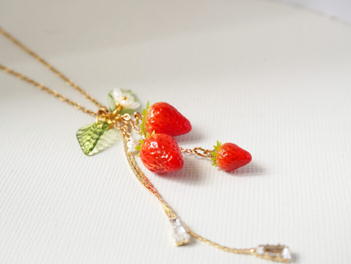 Close-up of three red polymer clay strawberry charms dangling together on a textured white background