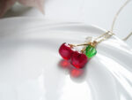 Resin cherry necklace pendant resting on a white plate, showing the flower, leaf, and chain clasp