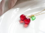Macro shot of two round red resin cherries and a green leaf charm on a white plate rim