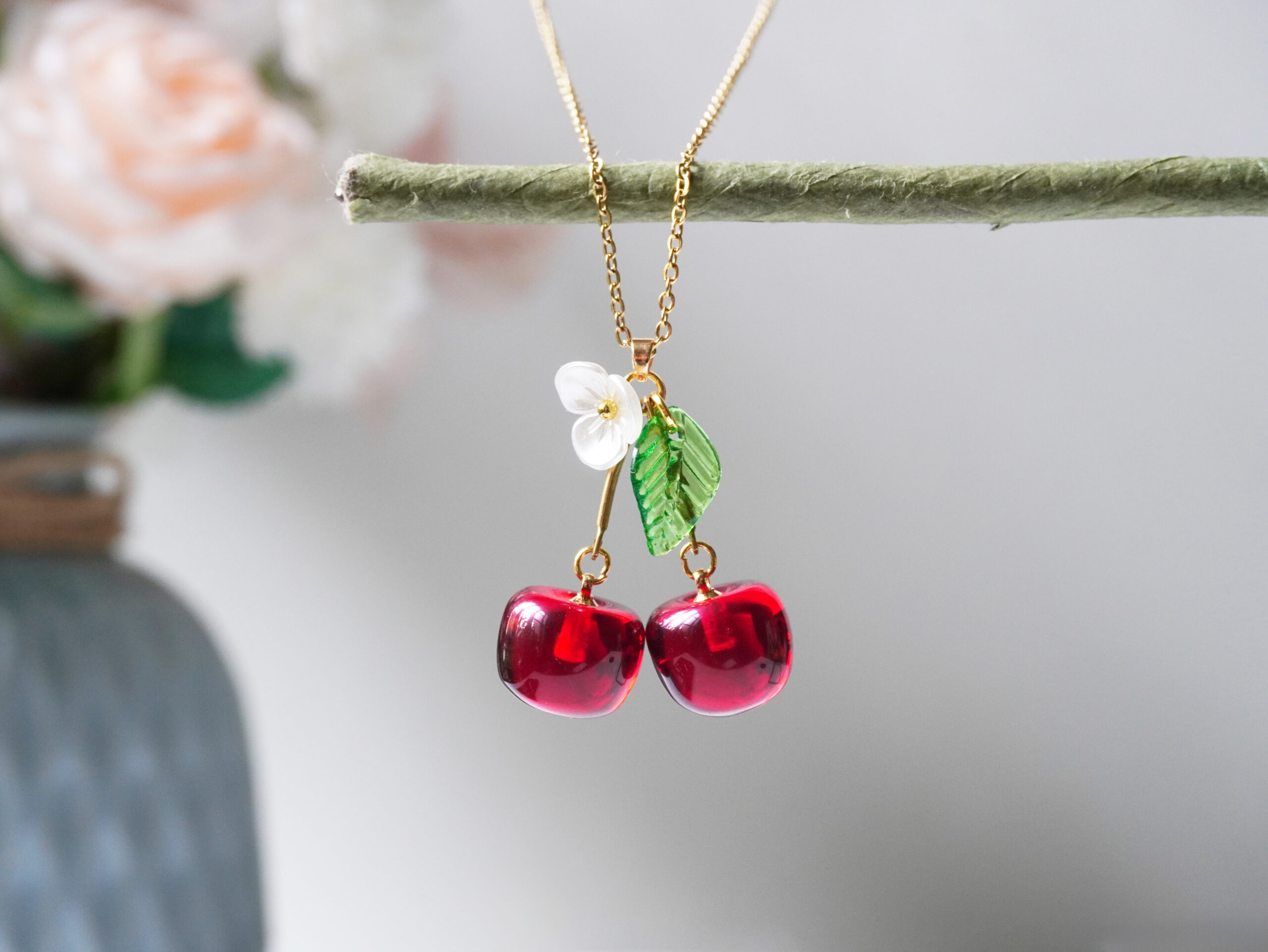 resin cherry necklace Resin cherry necklace hanging from a twig, showing gold chain, two cherries, and a delicate flower accent